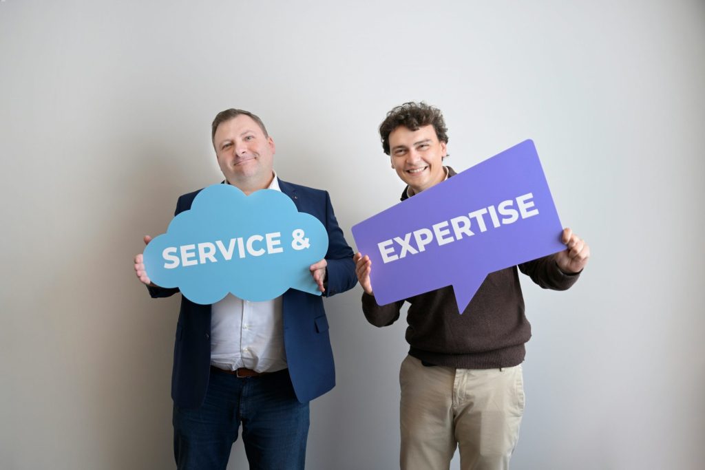 Two smiling men holding "service &" and "expertise" signs.