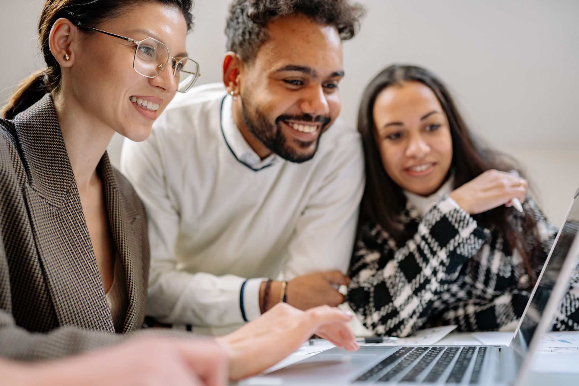 Three colleagues working together on a laptop in an office, showcasing diversity and teamwork.